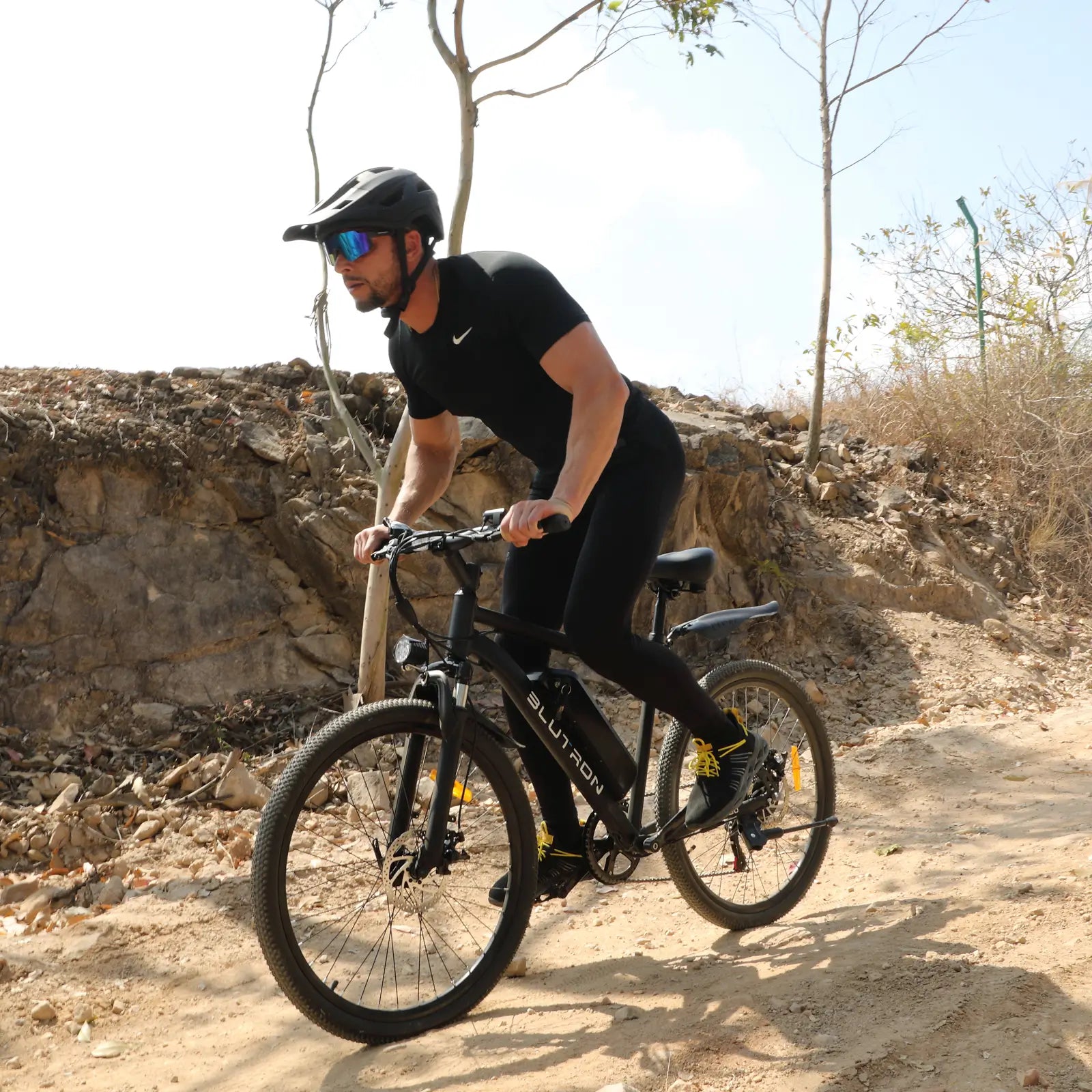 BLUTRON EB550 electric mountain bike: Rider navigating a rocky dirt trail, showcasing the bike’s detachable BLUTRON-branded battery — ideal for off-road use, set against a rugged outdoor backdrop