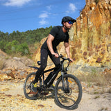 BLUTRON EB550 off-road ebike: Rider in athletic gear navigating rocky gravel terrain, featuring a detachable BLUTRON-branded battery — set against a rugged outdoor backdrop of cliffs and vegetation