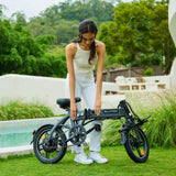 Woman folding a compact, BLUTRON ebike on a grassy outdoor area (pool backdrop) — this practical option is among folding ebikes for adults, highlighting its easy-to-use frame-folding structure