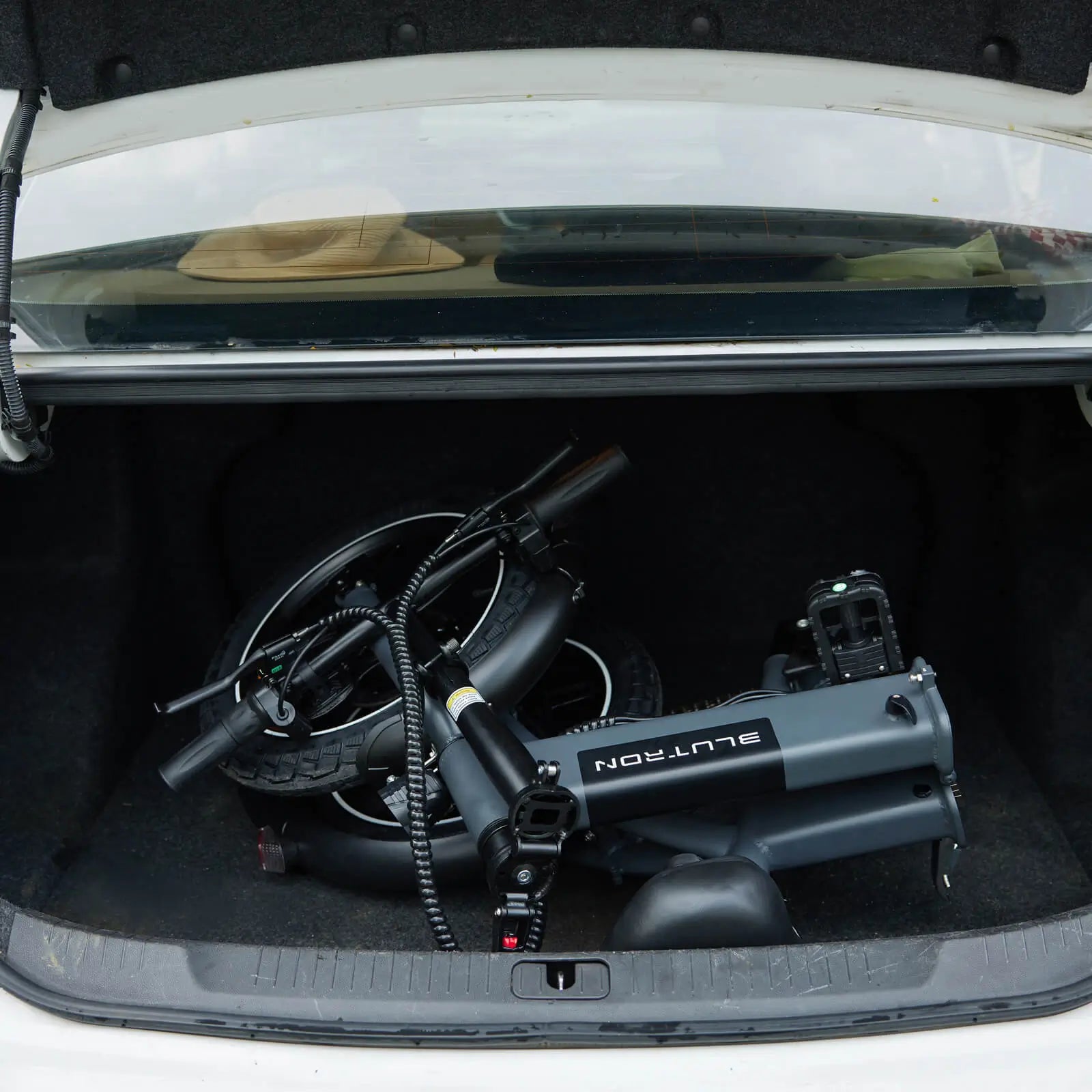 Blutron folding ebike 350w: Compact folded model stored in a car trunk, showcasing its space-saving design alongside visible tires and wiring components