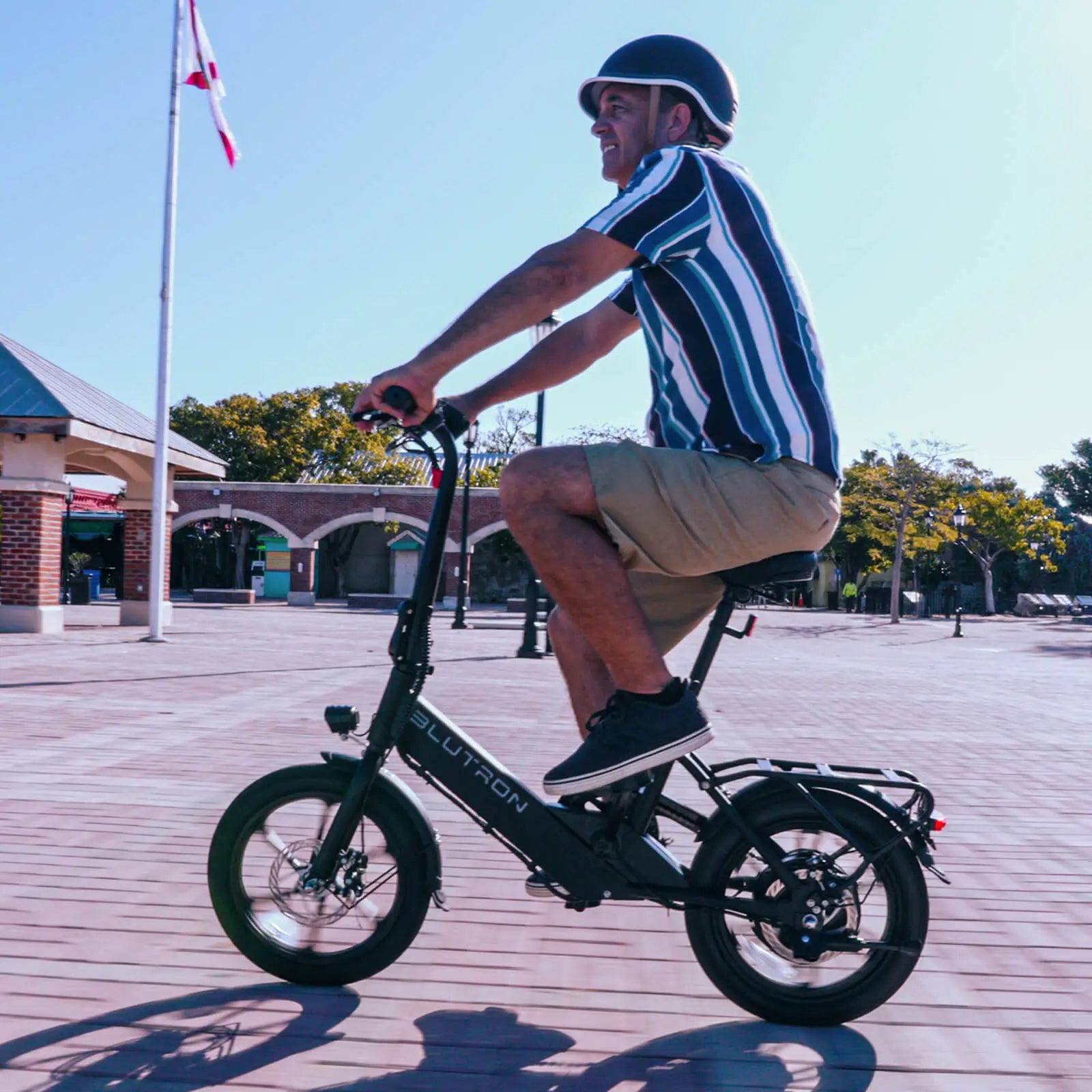 Helmeted rider glides a Blutron urban compact folding ebike on a brick plaza—fitted with front LED light, rear cargo rack.