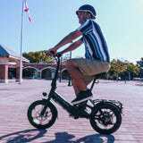 Helmeted rider glides a Blutron urban compact folding ebike on a brick plaza—fitted with front LED light, rear cargo rack.